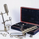 A microscope compendium containing many different parts in a portable case; microscopes are shown assembled in the foreground.