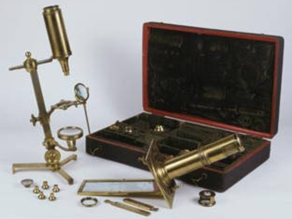 A microscope compendium containing many different parts in a portable case; microscopes are shown assembled in the foreground.