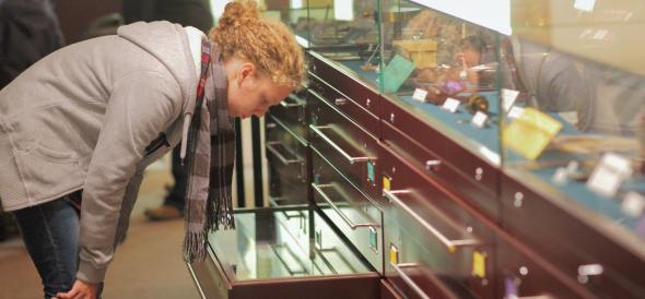 Woman looking into an open drawer below a museum display case.