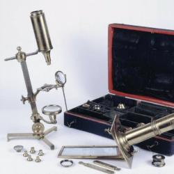 A microscope compendium containing many different parts in a portable case; microscopes are shown assembled in the foreground.