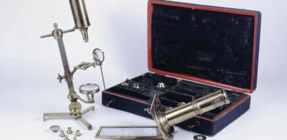 A microscope compendium containing many different parts in a portable case; microscopes are shown assembled in the foreground.